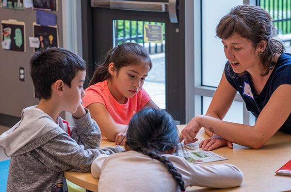 A teacher talks with three young students at a table.