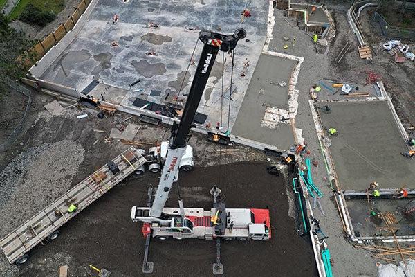 aerial view of a crane with workers attaching a piece of structural steel
